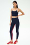 A woman wears the SPLITS59 Cait Rigor Bralette in Indigo/White with matching leggings and red Adidas sneakers, standing against a plain white background.