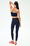 A woman faces away from the camera in a SPLITS59 Cait Rigor Bralette in indigo/white, paired with matching leggings and red sneakers, set against a plain white background.