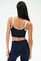 A woman is shown from the back wearing the SPLITS59 Cait Rigor Bralette in Indigo/White, paired with matching high-waisted leggings, both crafted from a soft nylon-spandex blend, against a plain background.