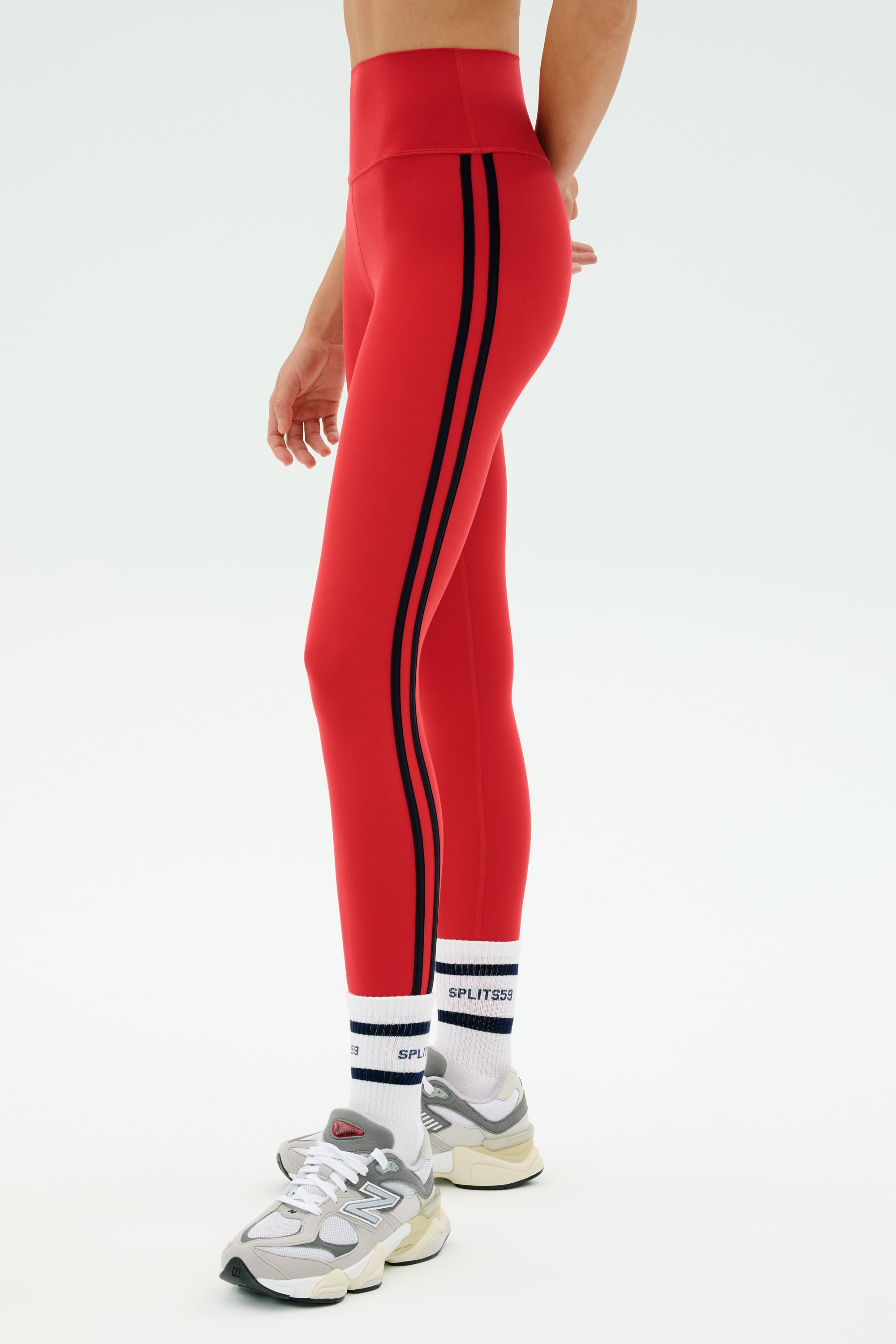 Person wearing SPLITS59 Ella High Waist Airweight 7/8 leggings in Pirate Red/Indigo, paired with white athletic socks and sneakers, standing against a plain light background.