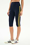 Someone sports SPLITS59’s Ella High Waist Airweight Capri in Indigo/Bright Yellow with white Adidas sneakers featuring navy stripes—a stylish, comfortable outfit perfect for hot yoga or active outings.