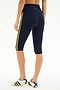 Model wears SPLITS59 Ella High Waist Airweight Capri in Indigo/Bright Yellow with white sneakers, shown from the back against a plain white background—ideal for hot yoga sessions.
