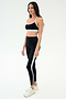 Woman in black SPLITS59 Emerson Airweight Bra - Black/Ice with white and light blue trim, standing slightly to the side against a plain white background—ideal for hot yoga or Pilates.
