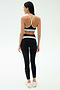 A woman faces away, wearing the SPLITS59 Emerson Airweight Bra in Black/Ice and high-waisted leggings with white accents, plus white sneakers—perfect for Pilates or hot yoga—set against a plain light background.