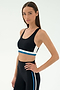 A woman wears the SPLITS59 Maci Airweight Bra in Black/Stone Blue with matching leggings, standing with one hand on her hip against a plain white background.
