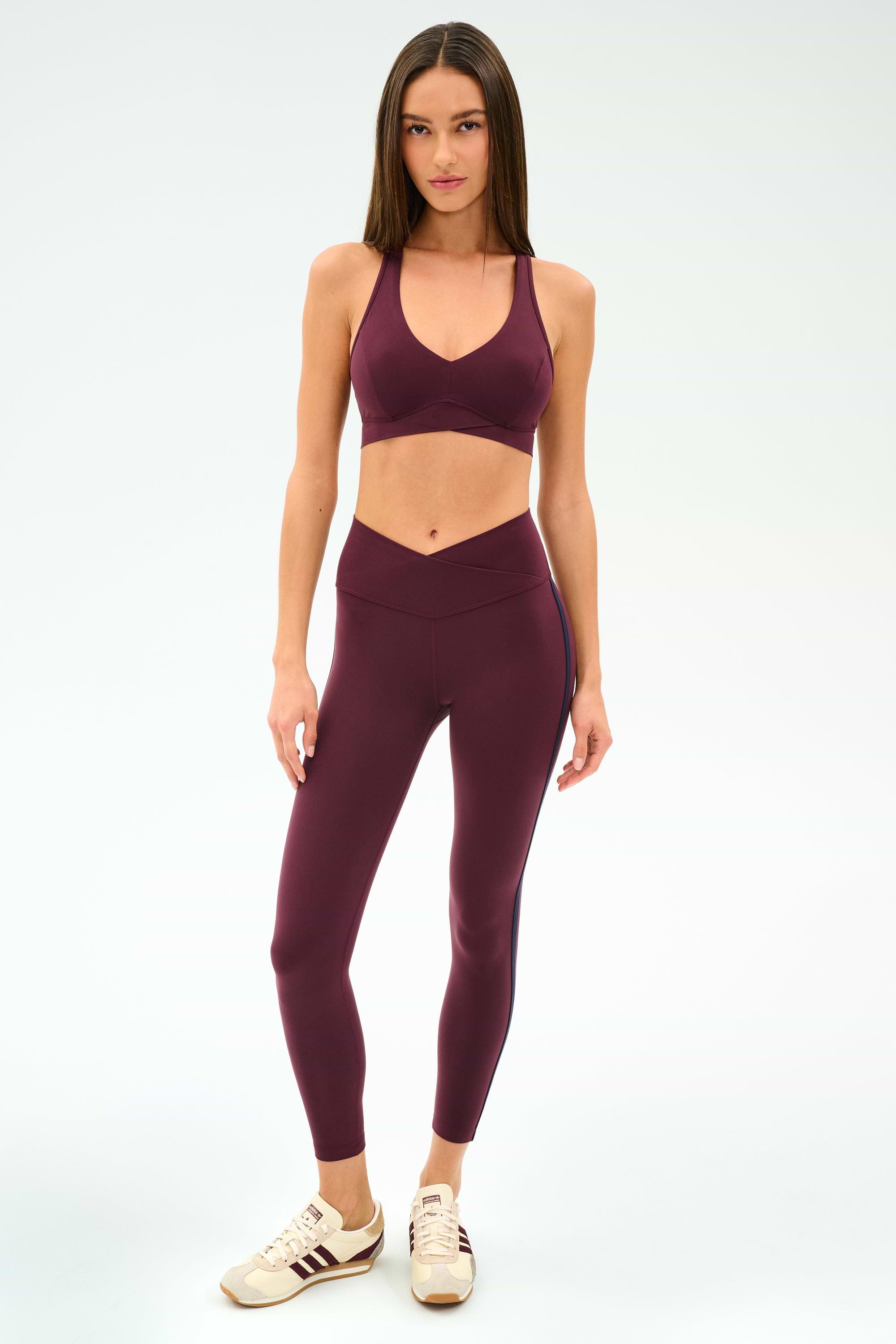 Woman wearing the SPLITS59 Mia Rigor Bra in Dark Cherry with matching leggings and beige sneakers, standing against a plain light background.