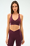 Woman stands against a plain background, wearing the SPLITS59 Mia Rigor Bra in Dark Cherry paired with matching high-waisted leggings.