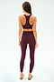 A woman faces away, wearing the SPLITS59 Mia Rigor Bra in Dark Cherry with matching leggings and light sneakers, set against a plain white background.