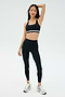 A woman poses in the SPLITS59 Miles Rigor Bra - Black/White, coordinated high-waisted leggings, and athletic sneakers—exuding comfort and style against a simple backdrop.