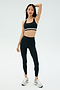A woman poses in the SPLITS59 Miles Rigor Bra - Black/White, coordinated high-waisted leggings, and athletic sneakers—exuding comfort and style against a simple backdrop.
