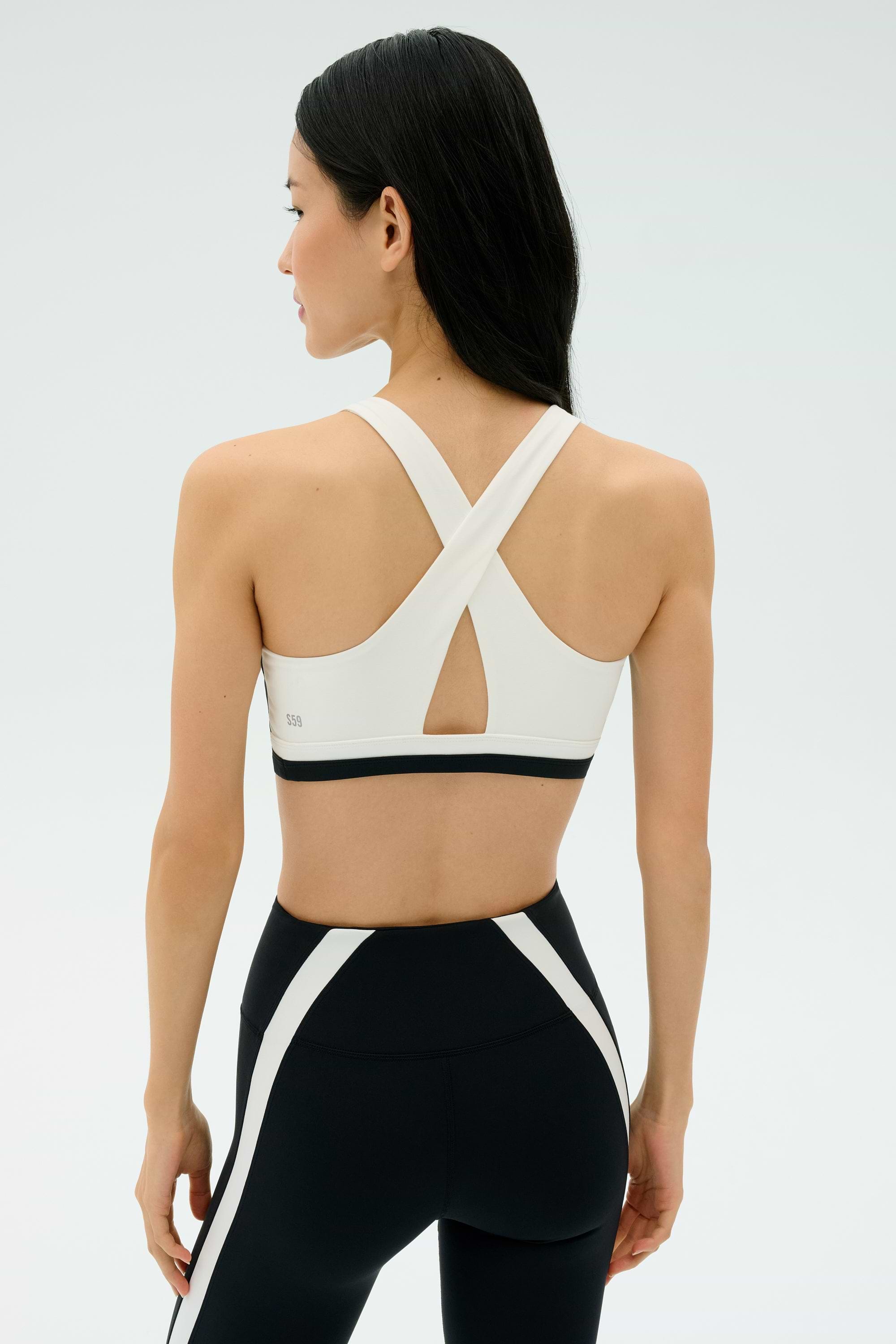 A woman stands with her back to the camera wearing the SPLITS59 Miles Rigor Bra - Black/White, paired with black athletic leggings featuring white accents—ideal for high-intensity gym workouts.