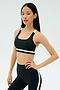 A woman poses in SPLITS59's Miles Rigor Bra - Black/White and matching leggings with white stripes, standing against a plain light background.