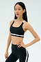 A woman poses in SPLITS59's Miles Rigor Bra - Black/White and matching leggings with white stripes, standing against a plain light background.