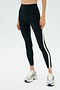 Person wears SPLITS59 Miles High Waist Rigor 7/8 leggings in Black/White with white side stripes and silver sneakers, standing against a plain light background.
