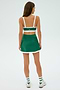 In a plain background, a person stands with their back to the camera, wearing a green athletic skirt, striped socks, and sneakers. They sport a SPLITS59 Monah Rigor Bra in Arugula/White, ready for gym workouts.