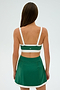 A woman is shown from the back, wearing an SPLITS59 Monah Rigor Bra in Arugula/White with a green skirt, ready for her gym workouts.