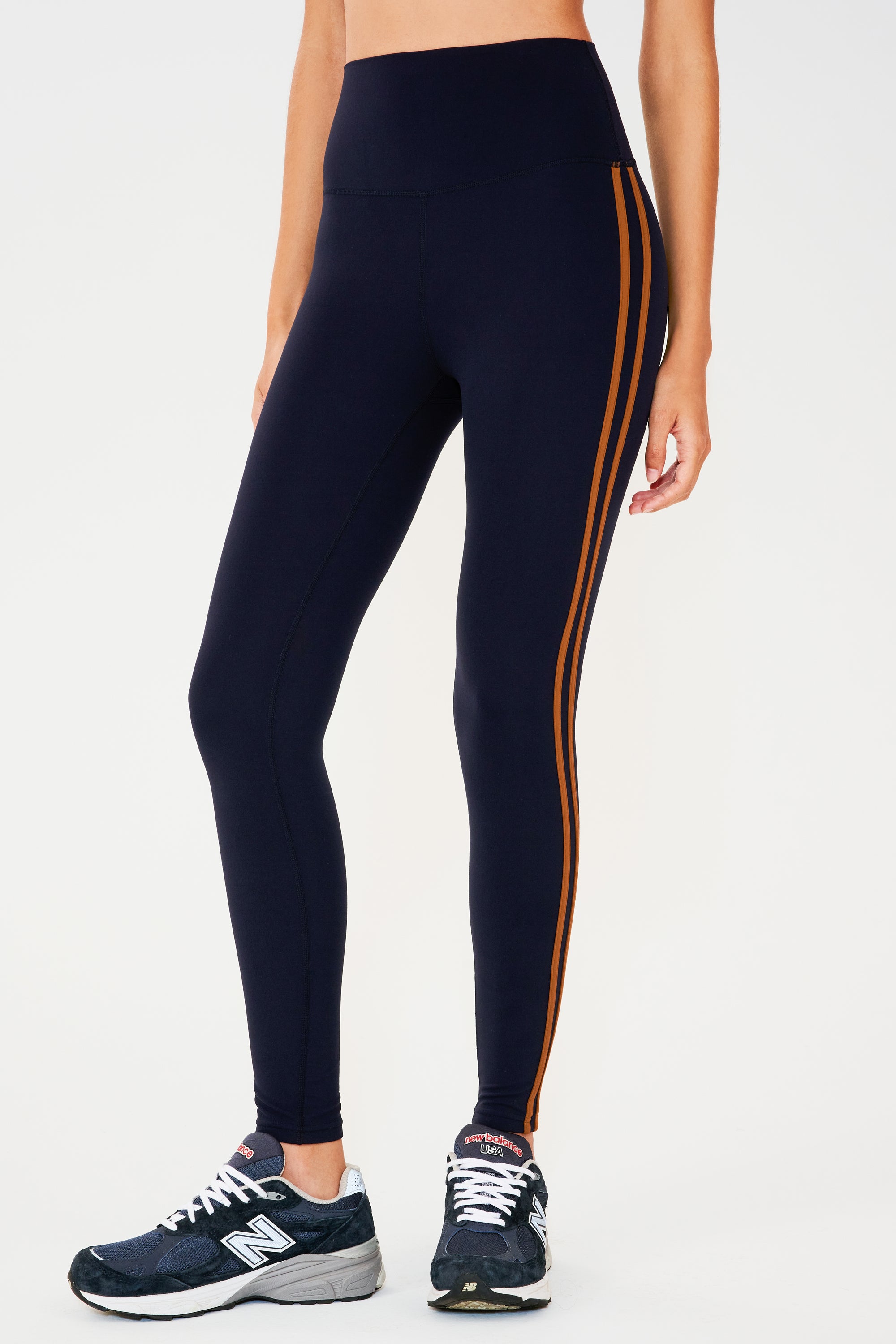 Side view of girl wearing dark blue leggings with two thin brown stripes down the side with dark blue shoes