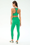 A woman faces away, wearing the SPLITS59 Amber Airweight High Waist 7/8 leggings in Spearmint/Military with white and black trim, paired with matching sports bra and green-white sneakers against a plain light background.