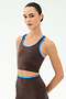 A woman wears the SPLITS59 Amber Airweight Bralette in Dark Chocolate/Classic Blue, featuring a scoop neck and matching high-waisted leggings, both crafted from performance Airweight fabric, standing against a plain light background.