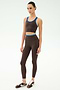 A woman models the SPLITS59 Amber Airweight Bralette in Dark Chocolate/Classic Blue, crafted from performance fabric perfect for hot yoga, with matching leggings and sneakers, posed against a white background.