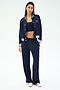 A woman wears the SPLITS59 Hayes Varsity Rigor Jacket in Indigo, paired with a matching crop top and loose stretch pants with white stripes, and white sneakers, standing against a plain light background.