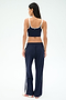 A woman, facing away, wears a navy blue crop top and SPLITS59 Maxie Rigor Track Pant in Indigo/White with white trim and side stripes, against a plain white background.