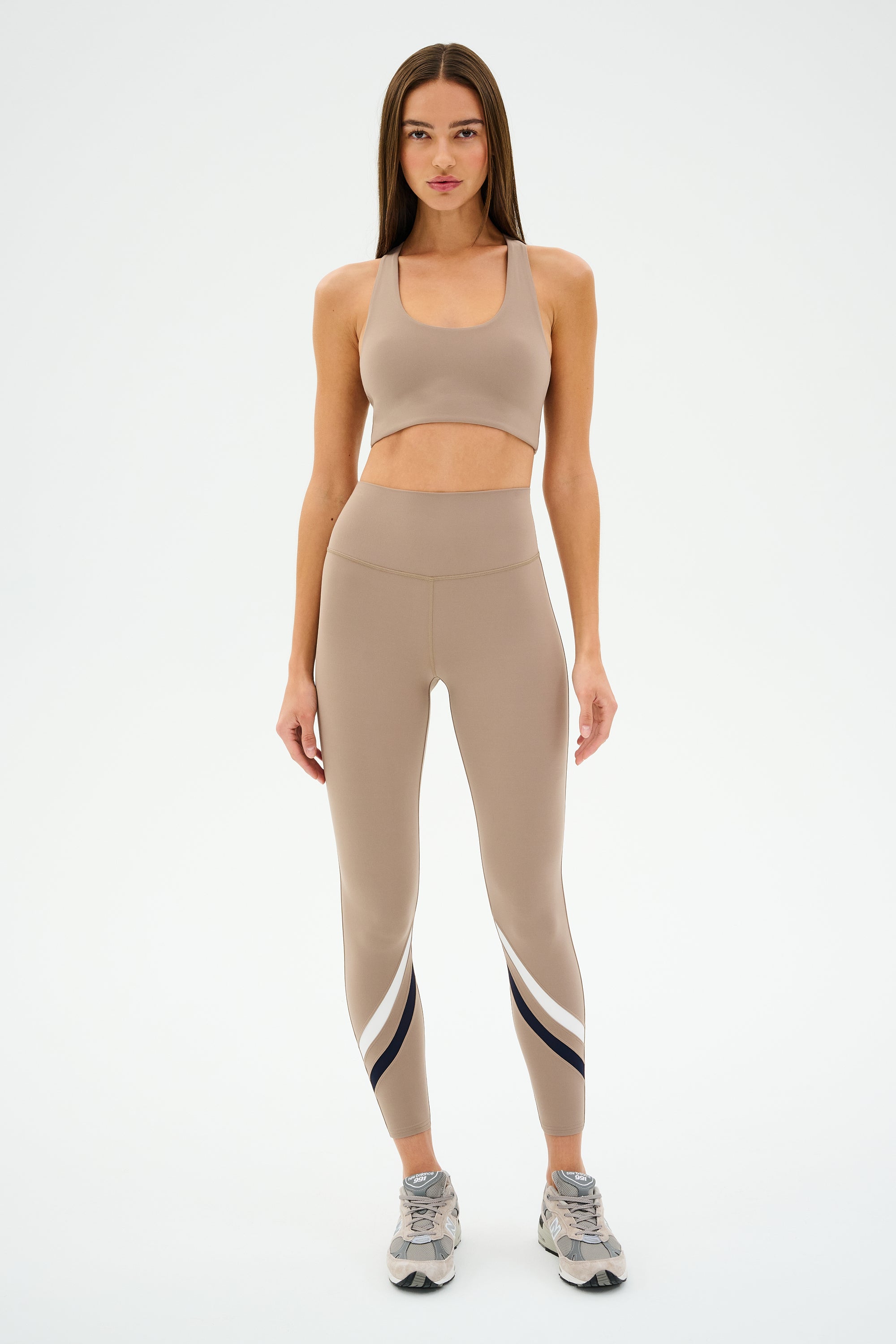 A person wearing SPLITS59's Chevron Airweight High Waist 7/8 leggings in Latte/Indigo and an ultra-luxe fabric sports bra stands on a white background.