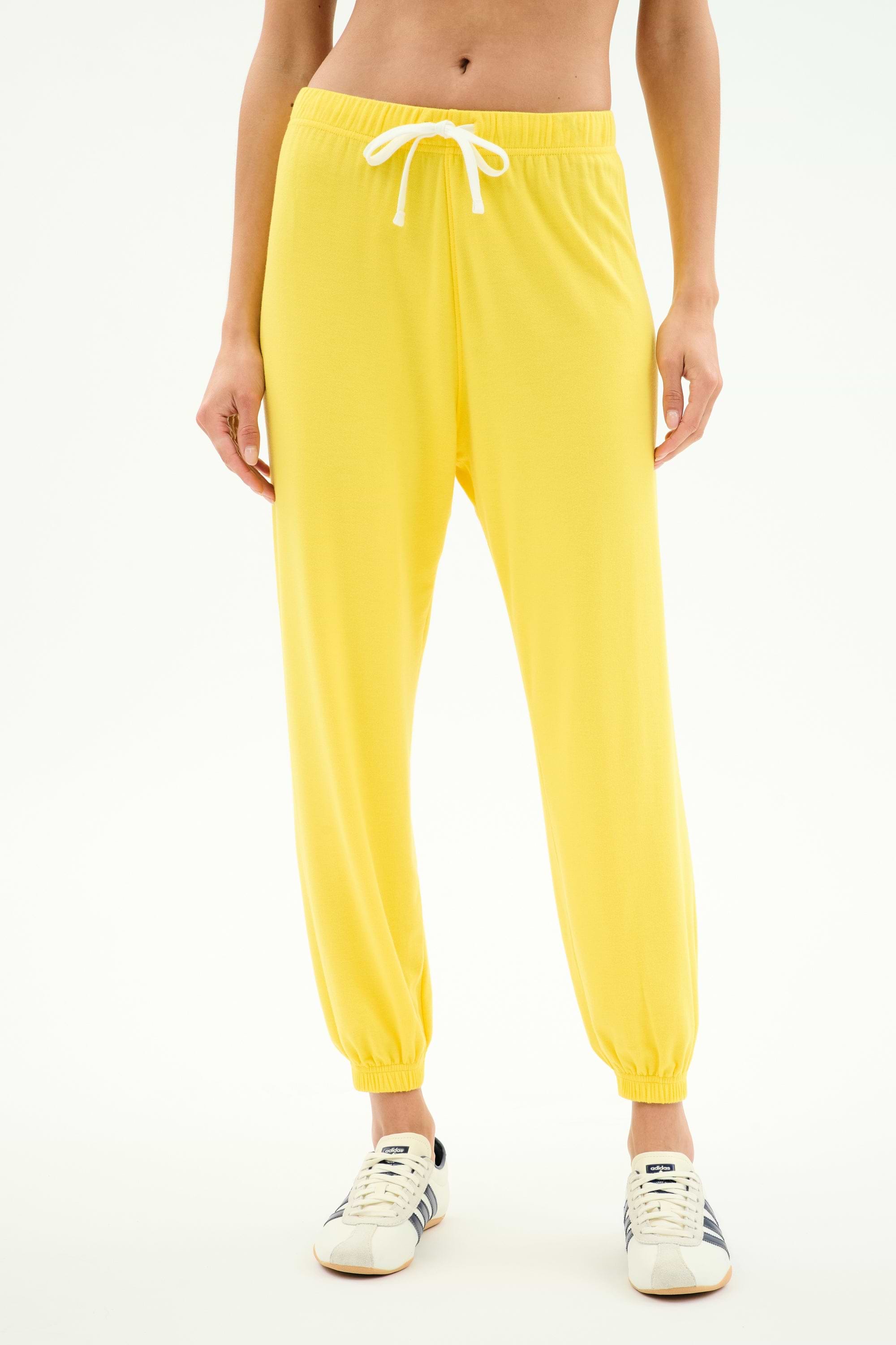 A person wears SPLITS59's Andie Oversized Fleece Sweatpant in bright yellow, featuring a white drawstring, paired with white sneakers and standing against a plain white background.