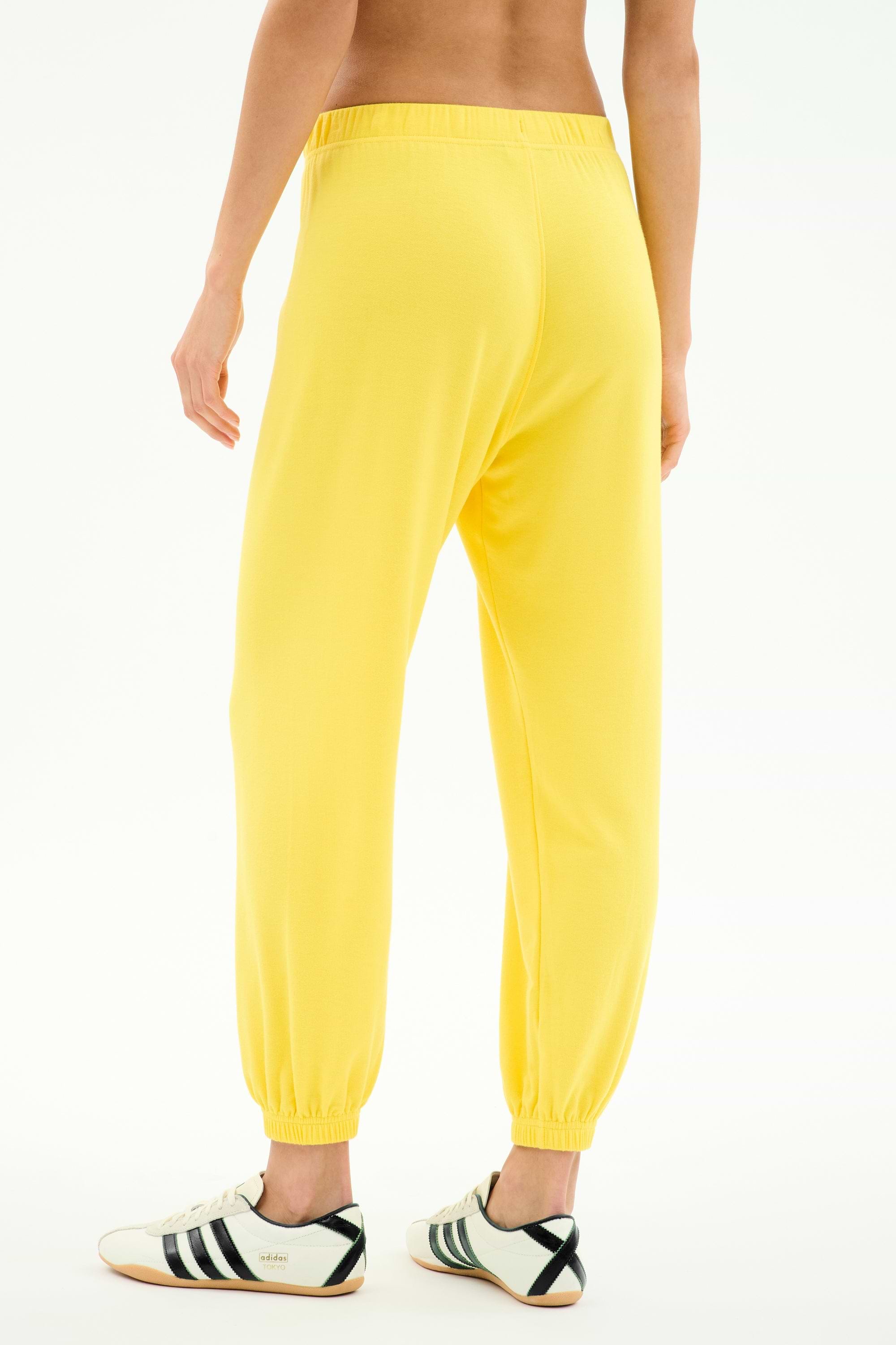 Model wears SPLITS59 Andie Oversized Fleece Sweatpant in bright yellow, paired with white sneakers with black stripes, shown from the back against a plain white background.