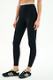 A person wearing SPLITS59 Dual High Waist Airweight 7/8 leggings in Black/White and black athletic shoes with white stripes, standing against a plain white background.