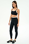 A woman stands against a white background wearing the SPLITS59 Dual High Waist Airweight 7/8 leggings in Black/White, paired with a black sports bra and black Adidas sneakers.
