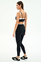 Woman standing sideways wearing the SPLITS59 Elliah Airweight Double Layer Bra in Black/White, paired with black spandex athletic wear and black Adidas sneakers, against a plain white background.