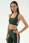 A woman models the SPLITS59 Lexi Rigor Bra in Military/Blush, featuring a dark green hue with pink and white side stripes, set against a plain light background.