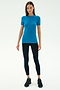 A woman stands facing forward wearing the SPLITS59 Louise Rib Short Sleeve in Stone Blue, black leggings with blue side stripes, and black athletic shoes—perfect for yoga or gym workouts against a white background.