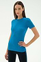 A woman stands against a plain background wearing the SPLITS59 Louise Rib Short Sleeve in Stone Blue and black pants, exuding confidence—perfect attire for yoga or gym workouts.