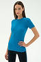 A woman stands against a plain background wearing the SPLITS59 Louise Rib Short Sleeve in Stone Blue and black pants, exuding confidence—perfect attire for yoga or gym workouts.