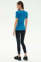 A woman faces away, wearing the SPLITS59 Louise Rib Short Sleeve in Stone Blue, paired with black leggings featuring white side stripes and black sneakers against a plain light background.