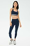 A woman stands against a plain background wearing the SPLITS59 Miles High Waist Rigor 7/8 leggings in Indigo/White with matching sports bra and silver athletic sneakers.