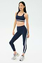 A woman wears the SPLITS59 Miles Rigor Bra in Indigo/White with matching leggings and gray sneakers, standing against a plain light background.