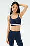 A woman wears the SPLITS59 Miles Rigor Bra in Indigo/White, standing against a plain light background with one hand on her head and a neutral expression.