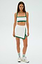 Person in a Monah Rigor Bra - White/Arugula sports outfit by SPLITS59, with a crop top and skirt, white sneakers, and matching socks, standing on a plain white background.