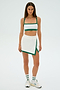Person in a Monah Rigor Bra - White/Arugula sports outfit by SPLITS59, with a crop top and skirt, white sneakers, and matching socks, standing on a plain white background.