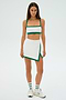 Someone is dressed in an SPLITS59 Monah Rigor Skort in White/Arugula, which includes a sports bra and skirt, against a plain background.