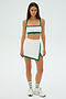 Someone is dressed in an SPLITS59 Monah Rigor Skort in White/Arugula, which includes a sports bra and skirt, against a plain background.