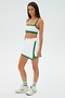 A person is dressed in the Monah Rigor Skort - White/Arugula by SPLITS59, featuring a sleeveless top and sneakers, against a plain white background.