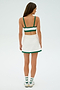 Facing away, a woman wears the SPLITS59 Monah Rigor Bra in white with green trim as part of a matching crop top and skirt set, paired with white socks and sneakers.