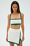 A person wearing the SPLITS59 Monah Rigor Bra in White/Arugula stands against a plain background, dressed in a white and green athletic outfit and skirt.