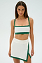 A person wearing the SPLITS59 Monah Rigor Bra in White/Arugula stands against a plain background, dressed in a white and green athletic outfit and skirt.