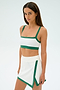 A person with long dark hair is wearing the Monah Rigor Bra in White/Arugula by SPLITS59, paired with a sporty skirt, standing against a plain light background.