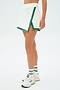 A person stands against a light background wearing the Monah Rigor Skort in White/Arugula from SPLITS59, complemented by white socks and athletic shoes with green accents.
